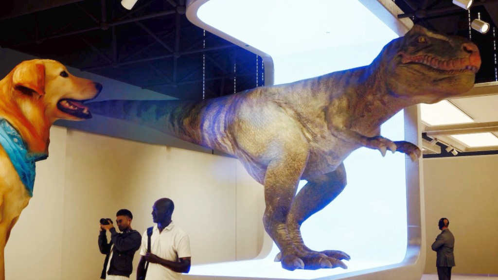 A white-walled modern art gallery with a live tyrannosaurus as an exhibit, visitors apparently oblivious to the danger. In the foreground there is another exhibit, a giant guide dog.