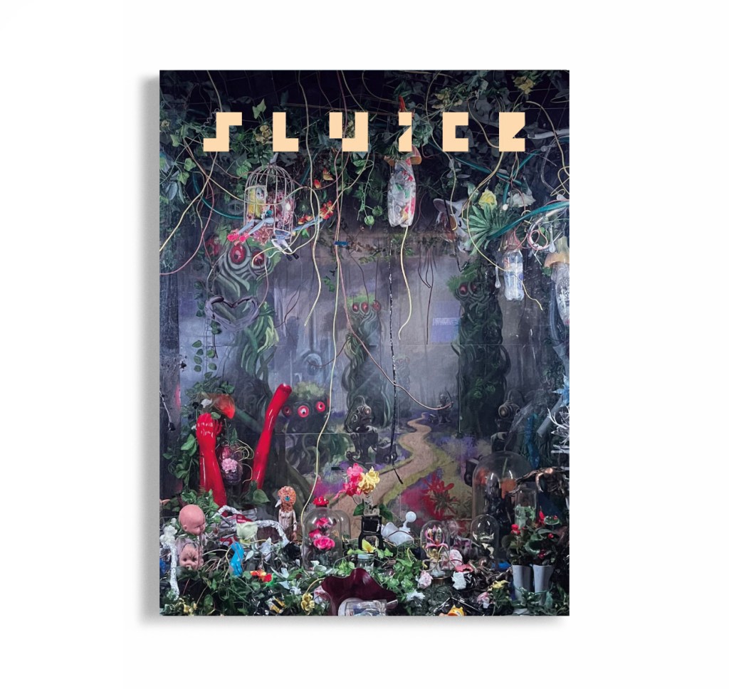 Cover of Sluice Magazine against a white background. The cover image is an installation of doll and mannequin parts intertwined with leaves and plants, against a painted backdrop showing a forest of tree-like creatures.