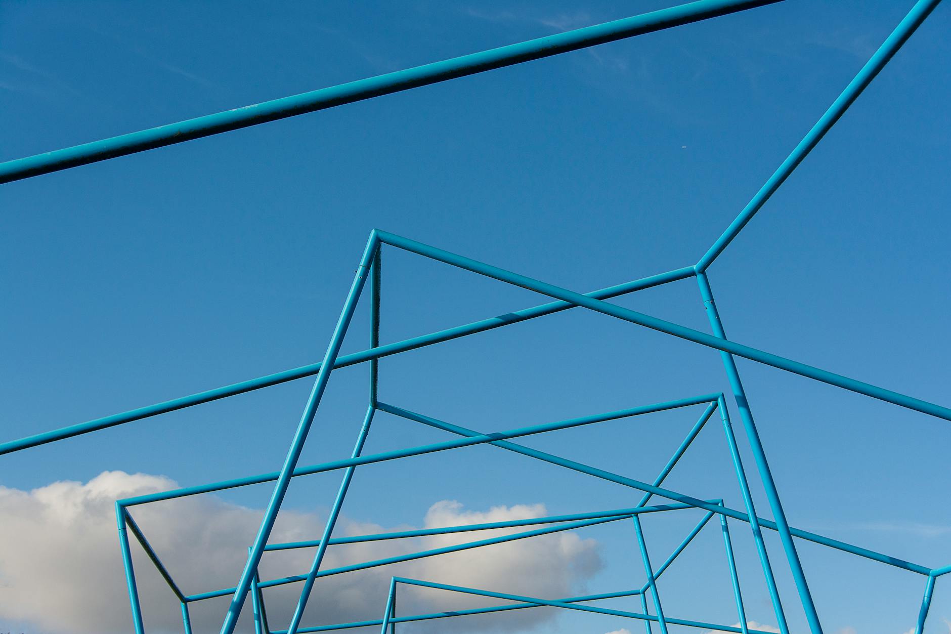 Blue metallic structure viewed from below, against a blue sky with a single white cloud in it.